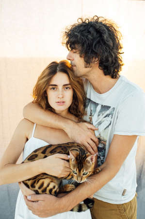 A handsome man with curly hair gently hugs his beloved. They have a cat in their handsの写真素材