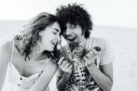 A handsome man with curly hair gently hugs his beloved. They have a cat in their handsの写真素材
