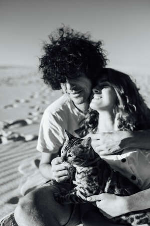 Cheerful young couple having fun on the beach with their bengal catの写真素材