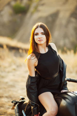 Girl on a motorcycle. She is beautiful, posing on a motorcycle at sunsetの写真素材