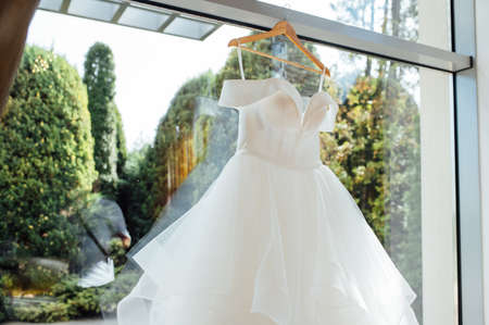 white Wedding dress hanging from a curtain pole with the sun shining through the windowの写真素材