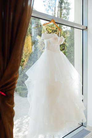 white Wedding dress hanging from a curtain pole with the sun shining through the windowの写真素材