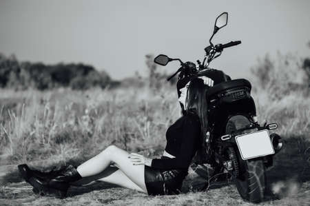 Beautiful girl in black clothes sits on motorcycle and poses for camera. Evening sunsetの写真素材