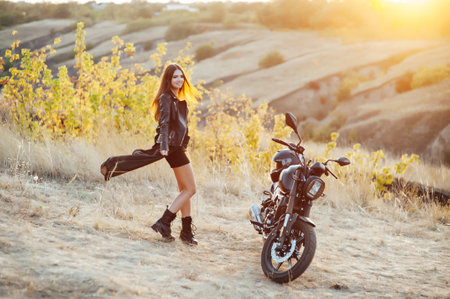 beautiful girl biker in black clothes dancing at the motorcycleの写真素材