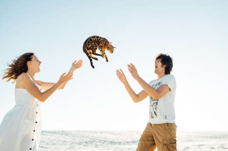 Cheerful young couple having fun on the beach with their bengal catの写真素材