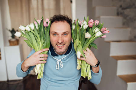 handsome man in a sweatshirt smiles and holds a bouquet of tulips in his handsの写真素材