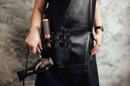 Person in black apron with professional hairdresser set on dark background, closeupの写真素材
