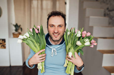 handsome man in a sweatshirt smiles and holds a bouquet of tulips in his handsの写真素材