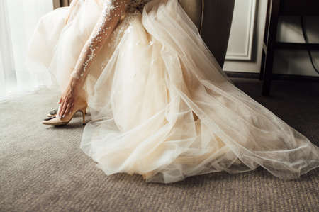 Bride with lace dress puts on her wedding shoes and straightens them with her handの写真素材