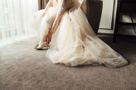 Bride with lace dress puts on her wedding shoes and straightens them with her handの写真素材
