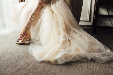 Bride with lace dress puts on her wedding shoes and straightens them with her handの写真素材