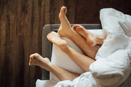 The feet of a young heterosexual couple relaxing in bed.の写真素材