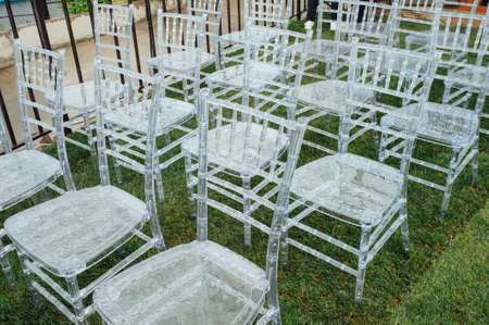 White glass chairs stand on the green grass. Round arch for a wedding ceremony In the background . Raining dayの写真素材