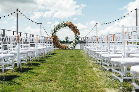 Round arch for a wedding ceremony by the river. White glass chairs stand for guests