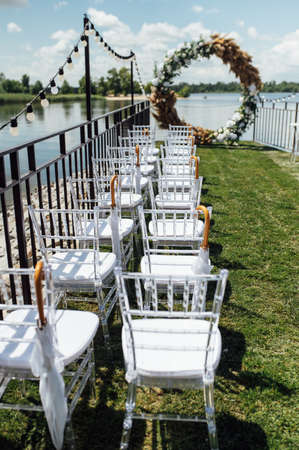 Round arch for a wedding ceremony by the river. White glass chairs stand for guestsの写真素材