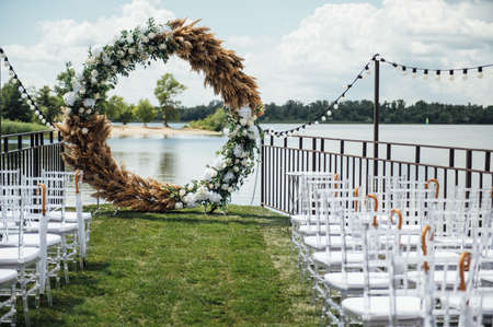 Round arch for a wedding ceremony by the river. White glass chairs stand for guestsの写真素材
