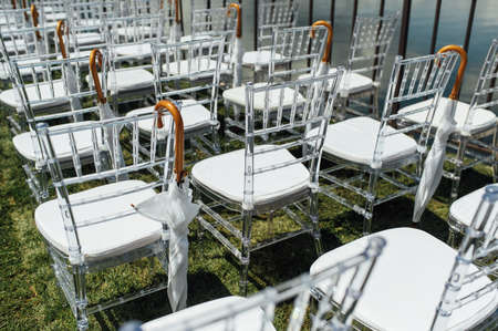 White glass chairs stand on the green grass. Round arch for a wedding ceremony in the backgroundの写真素材
