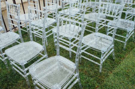 White glass chairs stand on the green grass. Round arch for a wedding ceremony In the background . Raining dayの写真素材
