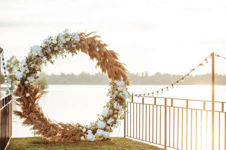 Round arch for a wedding ceremony by the river. White glass chairs stand for guestsの写真素材