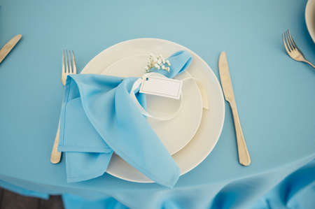Wedding tables for guests. Round tables with a blue tablecloth. Decorated with flowers, plates, glasses and moreの写真素材