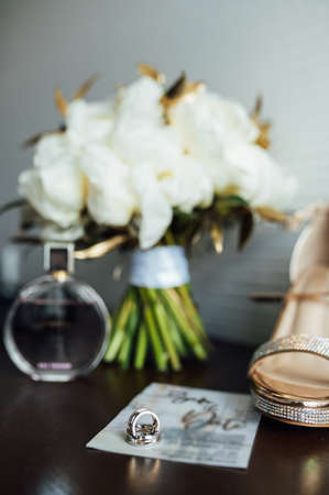 beautiful gold wedding rings on wooden table next to bouquet and shoesの写真素材