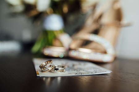 beautiful gold wedding rings on wooden table next to bouquet and shoesの写真素材