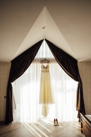 The brides dress hangs on the window. A gentle bouquet of the bride and womens shoes stand on the windowsillの写真素材