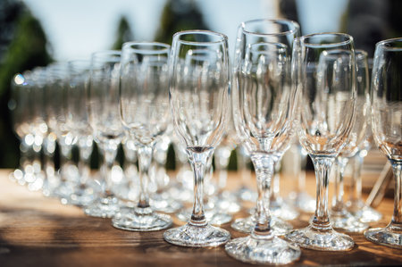 Row of empty champagne glasses on a table outdoors with sun reflection. Selective focus. Celebration conceptの写真素材