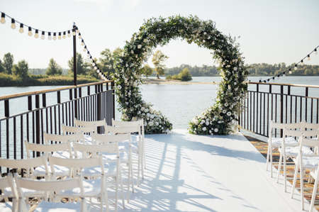 Circle wedding arch decorated with white flowers and greenery outdoors.の写真素材