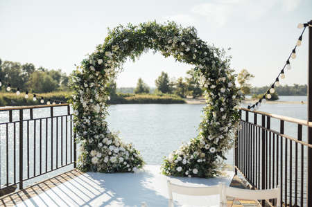 Circle wedding arch decorated with white flowers and greenery outdoors.の写真素材