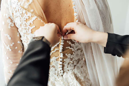 The bride puts on a white lace wedding dress, mom and girlfriend of the bride help to tie the dress from the back.の写真素材