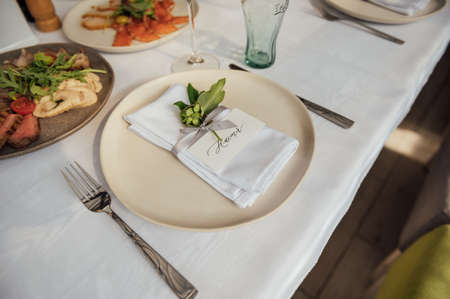 The festive table is served with plates with napkins and name cards, glasses and cutlery.