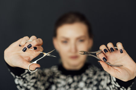 The nail master holds scissors and other tools in his hands. Beautiful blonde girlの写真素材