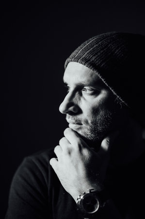 Serious dramatic man looking away while standing against black studio backgroundの写真素材
