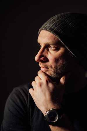 Serious dramatic man looking away while standing against black studio backgroundの写真素材