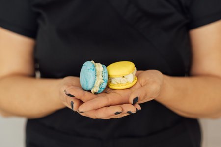 The confectioner is holding two yellow and blue French macarons in her hand. Ukrainian flag colorsの写真素材
