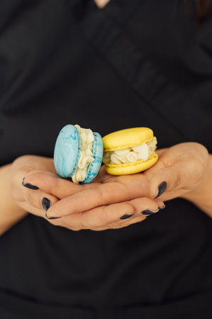 The confectioner is holding two yellow and blue French macarons in her hand. Ukrainian flag colorsの写真素材