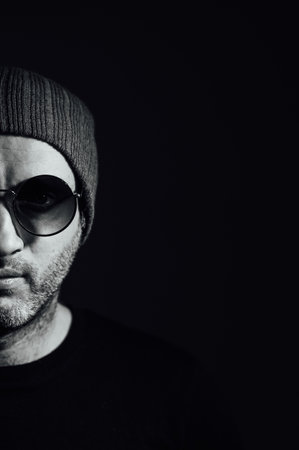 Serious dramatic man in sunglasses looking away while standing against black studio backgroundの写真素材