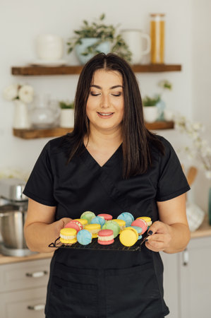 Woman confectioner holding traditional french colorful macarons in a rows on a metal meshの写真素材