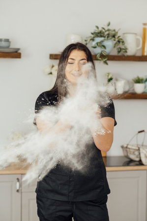 Woman baker clapping and sprinkling white flour over dough on kitchen backgroundの写真素材