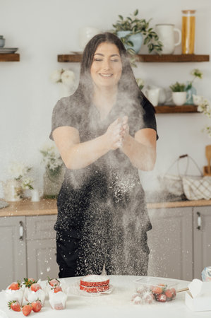 Woman baker clapping and sprinkling white flour over dough on kitchen backgroundの写真素材