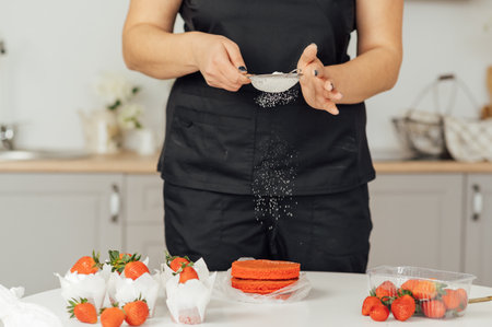 The cook sprinkles flour on a red cake through a sieveの写真素材