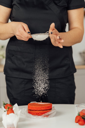 The cook sprinkles flour on a red cake through a sieveの写真素材