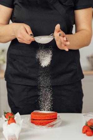 The cook sprinkles flour on a red cake through a sieveの写真素材