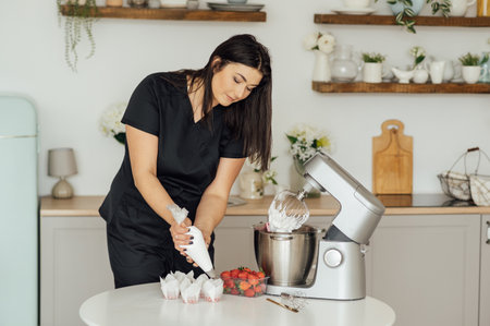 The girl cook puts the cream from the mixer into the mold for decorating cakesの写真素材