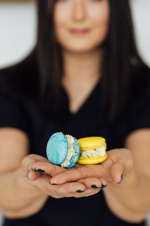 The confectioner is holding two yellow and blue French macarons in her hand. Ukrainian flag colorsの写真素材