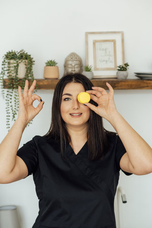 Smiling woman holding tasty colored macaron covering her eyesの写真素材