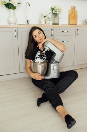 A woman cook sits on the floor and holds a professional mixer next to herの写真素材