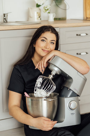 A woman cook sits on the floor and holds a professional mixer next to herの写真素材