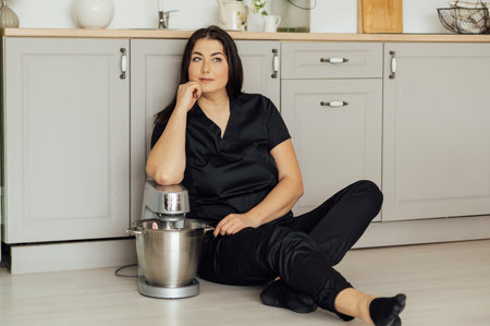 A woman cook sits on the floor and holds a professional mixer next to herの写真素材